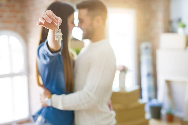 Casal jovem se mudando para uma nova casa, abraçando no amor mostrando chaves — Fotografia de Stock