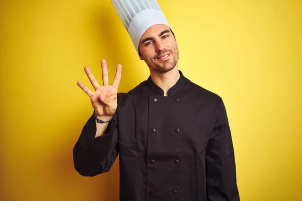 年轻的厨师 身穿制服 头戴帽子 站在孤立的黄色背景上 带着自信和快乐的笑容 用第四指尖 — 图库照片