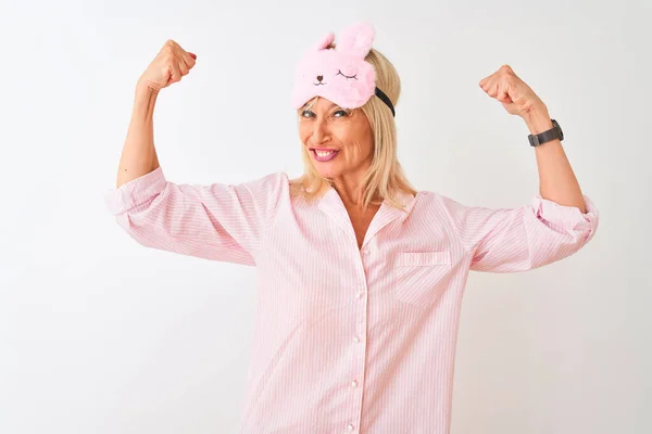 Middle age woman wearing sleep mask and pajama over isolated white background showing arms muscles smiling proud. Fitness concept.