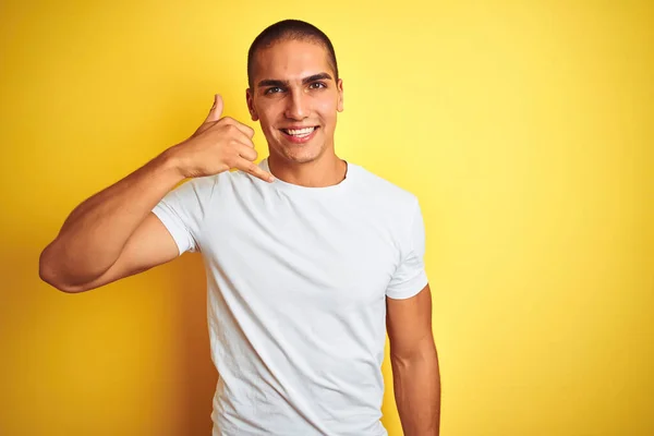 年轻的高加索男人穿着休闲的白色T恤 背景是黄色的孤立的 微笑着 用手和手指做着电话手势 就像在电话里说话一样 交流概念 — 图库照片