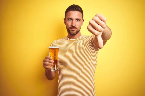 年轻英俊的男人喝了一品脱啤酒与孤立的黄色背景愤怒的脸 消极的迹象显示不喜欢拇指向下 拒绝的概念 — 图库照片