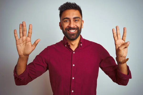 Young indian man wearing red elegant shirt standing over isolated grey background showing and pointing up with fingers number eight while smiling confident and happy.