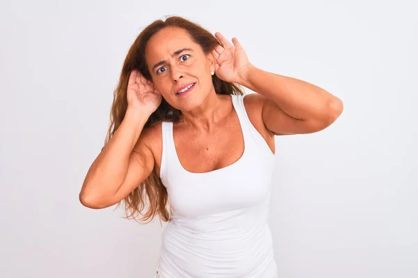 中年の成熟した女性が白い孤立した背景の上に立って耳のジェスチャーで両方の手を聞くしようとすると ゴシップを好奇心 聴覚障害 聴覚障害 — ストック写真