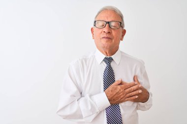 Kravat ve gözlük takan kıdemli gri saçlı işadamı izole edilmiş beyaz arka planda gülümsüyor elleri göğsünde, gözleri kapalı ve yüzünde minnet dolu bir jest ile. Sağlık kavramı.