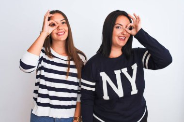 Genç ve güzel kadınlar günlük giysiler giyip izole edilmiş beyaz arka planda duruyorlar. El hareketleriyle gülümsüyorlar, gözleriyle mutlu yüzleriyle parmaklarının arasından bakıyorlar..