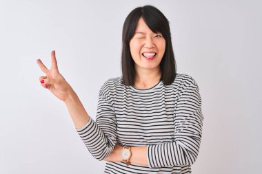 İzole edilmiş beyaz arka plan üzerinde siyah çizgili tişört giyen genç ve güzel Çinli kadın kameraya bakıp zafer işareti yaparken gülümsüyor. İki numara..