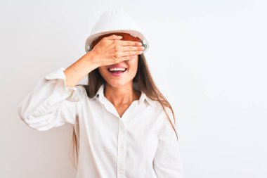 Kask ve gözlük takan genç, güzel bir mimar kadın izole edilmiş beyaz arka planda gülümsüyor ve yüzünde şaşkınlıktan gözleri kapayarak gülüyor. Kör kavram.