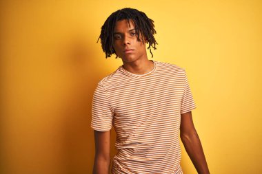 Rastalı tişörtlü Afro adam izole edilmiş sarı arka planda duruyor. Uykulu ve yorgun görünüyor. Yorgun ve akşamdan kalma..