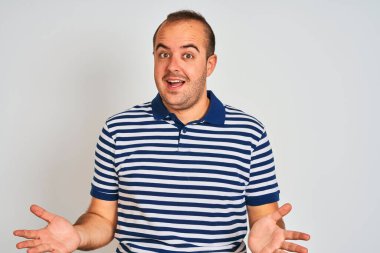 Sıradan çizgili polo giyen genç adam izole edilmiş beyaz arka planda dikiliyor. Neşeli gülümsüyor ve kollarını açıyor. Dostça karşılama, olumlu ve kendinden emin selamlar.
