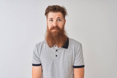 İzole edilmiş beyaz arka planda duran gri polo giyen genç kızıl saçlı adam yüzünde ciddi bir ifadeyle rahatlamış. Basit ve doğal bir şekilde kameraya bakıyorsun..