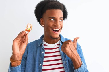 Genç Afro-Amerikalı adam yemek çubuklarıyla yemek yiyor. İzole edilmiş beyaz arka planda. Başparmağıyla gülümsüyor ve gülümsüyor.