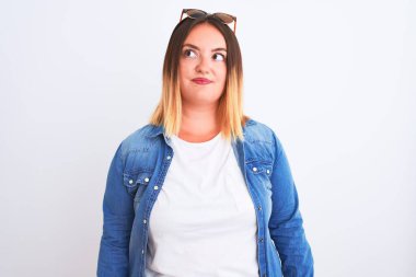 Güzel bir kadın kot gömlek giyiyor, beyaz arka plan üzerinde duruyor gülümsüyor ve yan tarafa bakıyor ve düşünüyor..