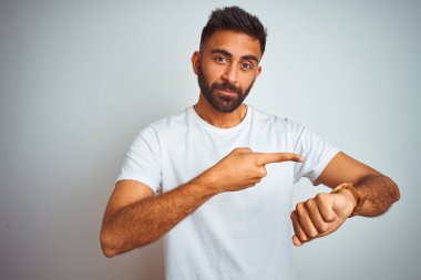 İzole edilmiş beyaz arka plan üzerinde duran genç Hintli adam saati, sabırsızlığı ve gecikmeye kızmayı işaret ederek acele ediyor.