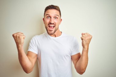 Yakışıklı delikanlı izole arka plan kutlama üzerinde rahat beyaz t-shirt giyen şaşırttı ve silah ile başarı için yükseltilmiş ve açık gözler hayrete düşürdü. Kazanan kavramı.