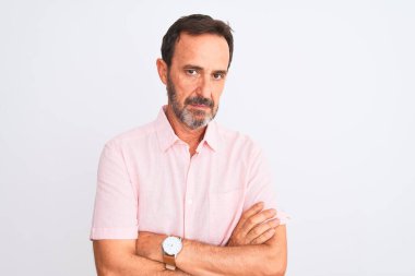 Orta yaşlı, pembe tişört giyen yakışıklı bir adam izole edilmiş beyaz arka plan üzerinde duruyor şüpheci ve gergin, yüzünde çapraz kollu tasvip etmeyen bir ifade. Negatif kişi.