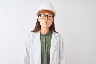 Genç Çinli mühendis kadın, izole edilmiş beyaz arka planda ceket kaskı gözlüğü takıyor dudaklarıyla balık suratı yapıyor, çılgınca ve komik bir jest. Komik ifade.