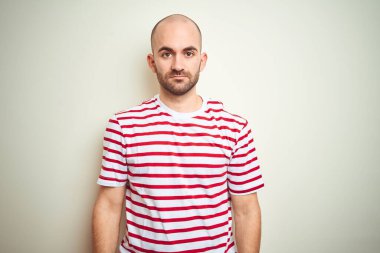 Sakallı, beyaz izole edilmiş arka plan üzerine normal çizgili kırmızı tişört giyen genç kel bir adam. Yüzünde ciddi bir ifadeyle rahatlamış. Basit ve doğal bir şekilde kameraya bakıyorsun..