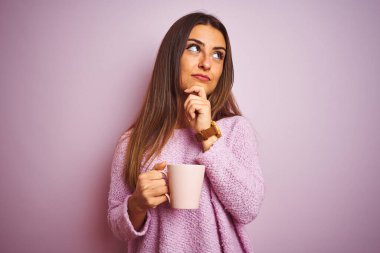 Genç, güzel bir kadın bir fincan kahve içiyor pembe arka planda dikiliyor ciddi bir yüz düşünüyor soru soruyor, çok karışık bir fikir.