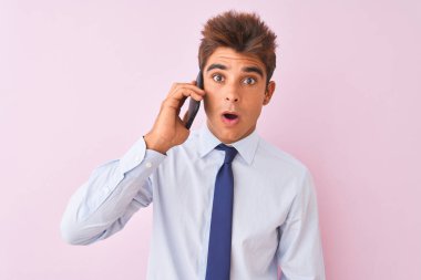 Akıllı telefondan konuşan genç ve yakışıklı bir iş adamı. Pembe arka planda. Şaşırmış bir yüzle korkmuş ve korku ifadesiyle heyecanlanmış.