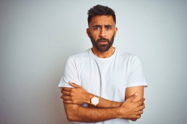 İzole edilmiş beyaz arka planda duran tişört giyen genç Hintli adam kış soğuğu için titriyor ve donuyor, yüzünde üzgün ve şok ifadesi var.