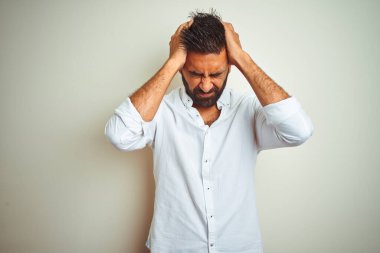 Zarif bir gömlek giyen genç Hintli adam izole edilmiş beyaz arka planda dikiliyor. Ağrı ve migrenden dolayı çaresiz ve stresli bir baş ağrısı çekiyor. Ellerini başının üstüne koy..