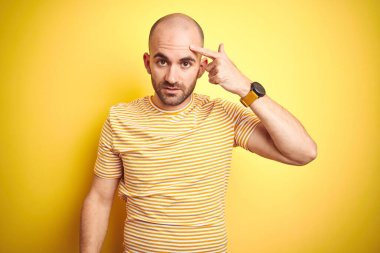 Sakallı, sarı renkli tişörtlü genç ve kel bir adam alnında sivilceden hoşlanmadığını gösteriyor. Siyah noktalı çirkin bir enfeksiyon. Sivilce ve deri problemi