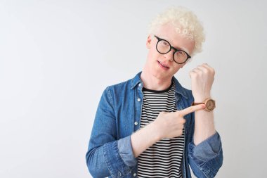 İzole edilmiş beyaz arka plan üzerinde kot gömlek ve gözlük takan genç albino sarışın adam. Aceleyle saati, sabırsızlığı ve rahat bir ifadeyle kameraya bakıyor.