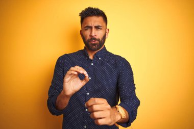 Genç, yakışıklı Hintli işadamı, izole edilmiş sarı arka plan iğrenç ifadesi üzerine gömlek giyiyor. Tiksinti tepkisi yüzünden tiksinti ve korku ifadesi takınıyor. Eller havada. Can sıkıcı bir kavram..