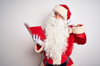 Orta yaşlı bir adam Noel Baba kostümü giyip izole edilmiş beyaz arka planda kitap okuyor. Telefonda el ve parmaklarıyla telefonla konuşuyor gibi gülümsüyor. İletişim kavramları.