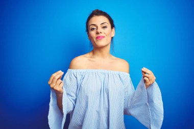 Genç, güzel bir kadın, mavi izole edilmiş arka planda çörek saç stili giyiyor. Elleriyle para jesti yapıyor, maaş ödemesi istiyor, milyonerlik işi yapıyor.