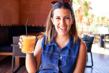 Genç ve güzel bir kadın restoranda oturmuş yaz tatilinin tadını çıkarıyor sağlıklı meyve suyu içiyor.