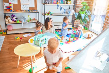 Güzel öğretmen ve bir grup çocuk anaokulunda bir sürü oyuncakla oynuyorlar.