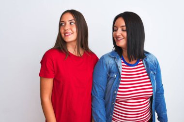 İzole edilmiş beyaz arka plan üzerinde sıradan kıyafetler giyen genç ve güzel kadınlar yüzünde gülümsemeyle, doğal bir ifadeyle yan yana bakıyorlar. Kendinden emin gülen.