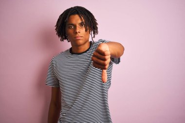 Rasta desenli tişörtlü Afro adam izole edilmiş pembe arka planda dikiliyor mutsuz ve kızgın görünüyor reddedilmiş ve olumsuz jest yapıyor. Kötü ifade.