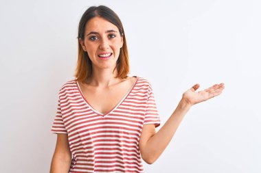 Güzel kızıl saçlı kadın izole edilmiş arka planda günlük kırmızı tişört giyiyor neşeli bir şekilde gülümsüyor ve avuç içi kameraya bakıyor..