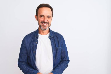 Orta yaşlı, mavi kot gömlek giyen yakışıklı adam izole edilmiş beyaz arka plan üzerinde el ele tutuşmuş ve parmaklarını çapraz yapıp gevşemiş ve neşeli gülümsüyor. Başarı ve iyimser