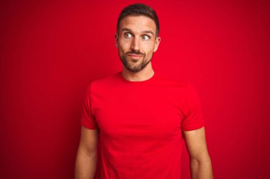 Kırmızı izole edilmiş arka planda rahat tişört giyen genç yakışıklı adam gülümsüyor ve başka yöne bakıyor..