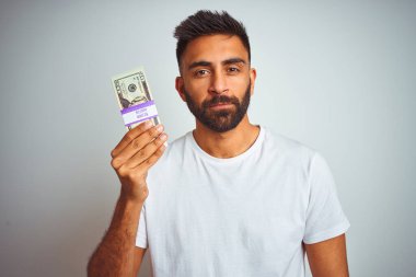 Soyutlanmış beyaz arka planda dolarları elinde tutan genç Hintli bir adam. Zeki bir yüz ifadesiyle ciddi olduğunu düşünüyor.