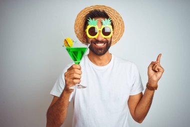 Yazın komik giyinen Hintli adam izole edilmiş beyaz arka planda kokteyl içerken çok mutlu görünüyor.