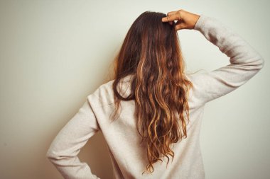 Kış süveteri giyen genç ve güzel bir kadın izole edilmiş beyaz arka planda dikiliyor. Elleri havada şüpheyi düşünüyor.