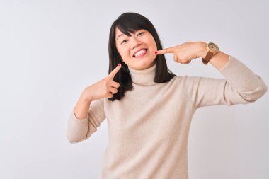 Genç, güzel, balıkçı yaka kazak giyen, izole edilmiş beyaz arka plan üzerine gülümseyen, parmaklarını, dişlerini ve ağzını gösteren güzel bir Çinli kadın. Diş sağlığı konsepti.