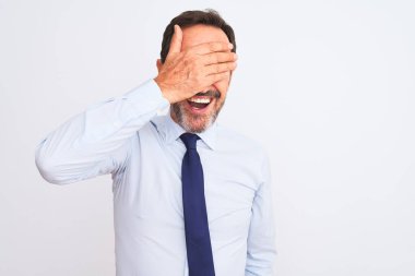 Orta yaşlı işadamı zarif bir kravat takıyor, izole edilmiş beyaz arka plan üzerinde duruyor, gülümsüyor ve elleri yüzünde şaşkınlıktan gözleri kapatıyordu. Kör kavram.