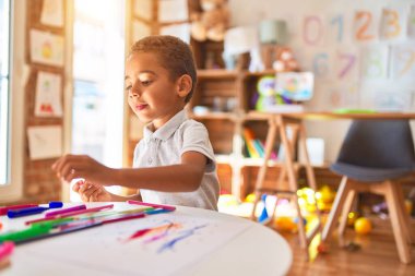 Güzel Afrikalı Amerikalı çocuk anaokulunda kağıt ve kalem kullanarak resim çiziyor.