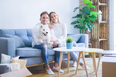 Karton kutular etrafında yeni evde kanepede oturan köpek ile genç güzel çift
