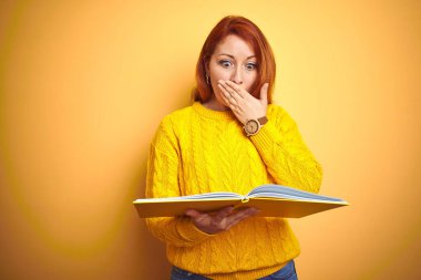 Genç, kızıl saçlı, kitap okuyan, sarı izole edilmiş arka plan kapağı üzerinde duran, utancından ağzı açık, korkunun ifadesi, sessizlikten korkan, gizli bir konsept.