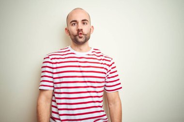 Sakallı, beyaz izole edilmiş arka planda sıradan kırmızı tişörtlü genç, kel bir adam dudaklı, çılgın ve komik yüzlü bir balık suratı yapıyor. Komik ifade.