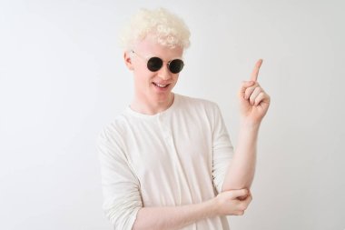 İzole edilmiş beyaz arkaplanda güneş gözlüğü ve tişört giyen genç albino bir adam. Yüzünde kocaman bir gülümseme var. Elleri ve parmakları kameraya bakıyor..