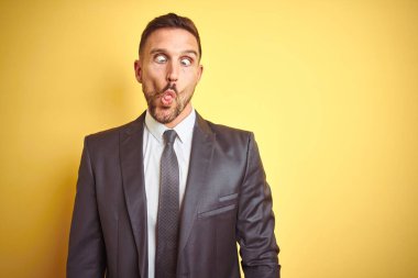 Genç yakışıklı iş adamı sarı arka planda kaldı. Dudaklarıyla balık suratı yapıyor. Çılgınca ve komik bir jest. Komik ifade.