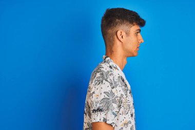 Tatilde olan Hintli genç bir adam, Hawaii gömleği giyiyor. İzole edilmiş mavi arka plan üzerinde duruyor. Yan tarafa bakıyor..
