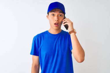 Akıllı telefondan konuşan şapkalı Çinli bir teslimatçı şaşırmış bir yüzle korkmuş ve korku ifadesinden heyecanlanmış bir şekilde izole edilmiş beyaz bir arka planda konuşuyordu.